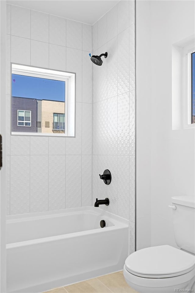 bathroom featuring toilet, tiled shower / bath combo, and tile patterned flooring