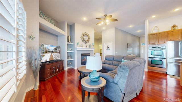 living room with built in shelves, ceiling fan, and dark hardwood / wood-style floors