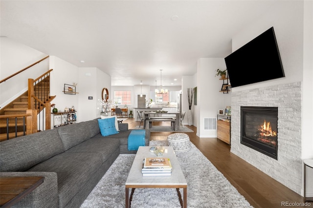 living room with visible vents, dark wood-type flooring, stairway, a stone fireplace, and a notable chandelier