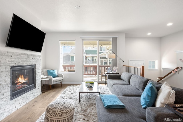 living room featuring a stone fireplace, recessed lighting, baseboards, and wood finished floors