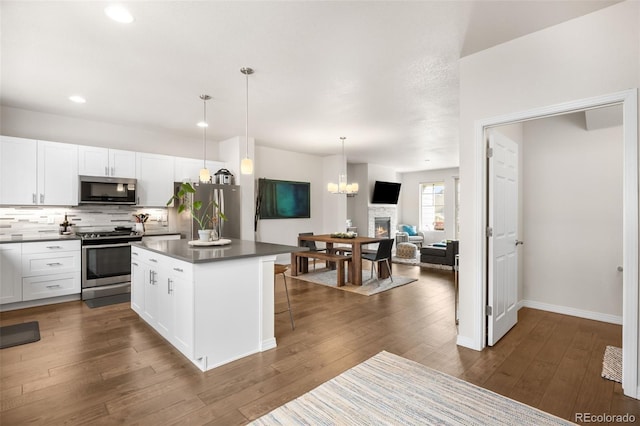 kitchen with tasteful backsplash, dark countertops, dark wood-type flooring, appliances with stainless steel finishes, and white cabinetry