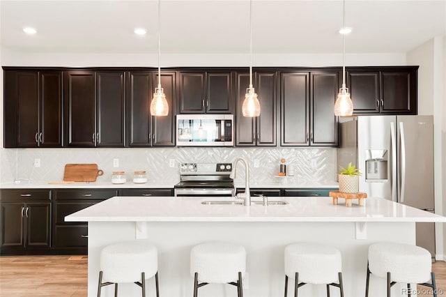 kitchen with sink, an island with sink, stainless steel appliances, and decorative light fixtures