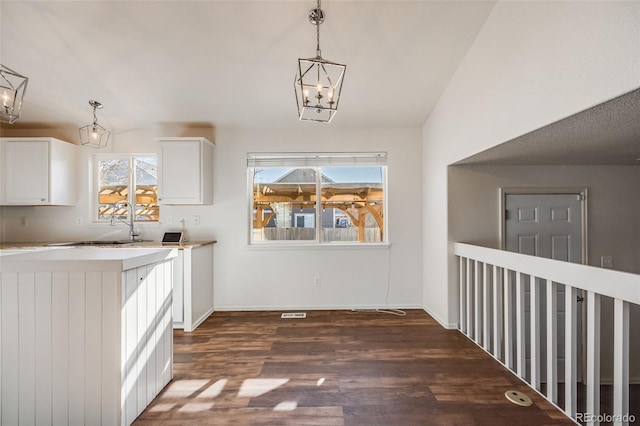 interior space with hanging light fixtures, plenty of natural light, dark wood-type flooring, and white cabinets