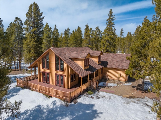 snow covered back of property with a wooden deck, roof with shingles, and french doors