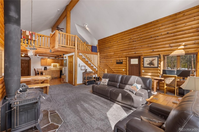living area featuring rustic walls, a wood stove, a ceiling fan, stairs, and high vaulted ceiling