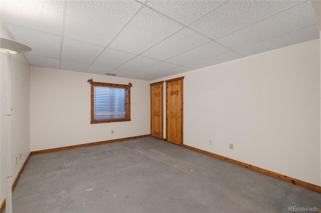 empty room with concrete floors, a drop ceiling, and baseboards
