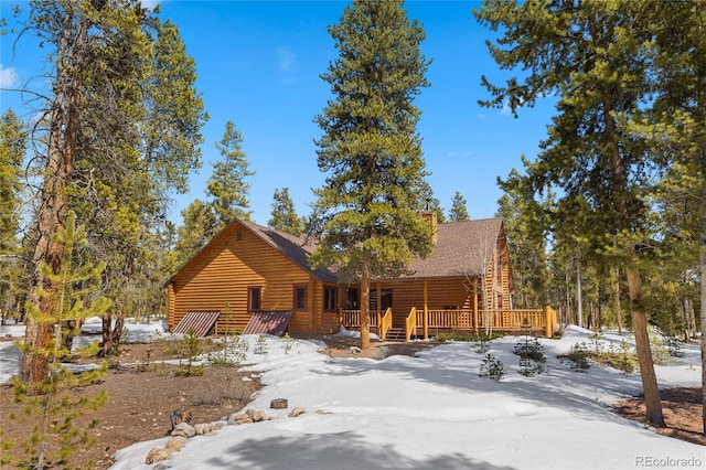 snow covered property featuring faux log siding and a deck