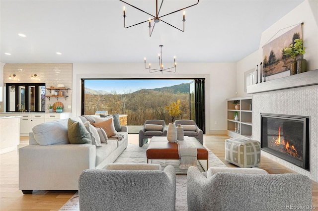 living room featuring baseboards, recessed lighting, light wood-style flooring, an inviting chandelier, and a glass covered fireplace