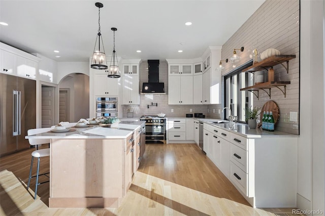 kitchen with light wood-style flooring, arched walkways, wall chimney range hood, premium appliances, and a center island