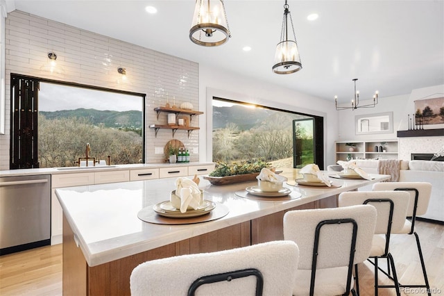 kitchen featuring stainless steel dishwasher, light wood-style floors, a notable chandelier, white cabinetry, and a sink