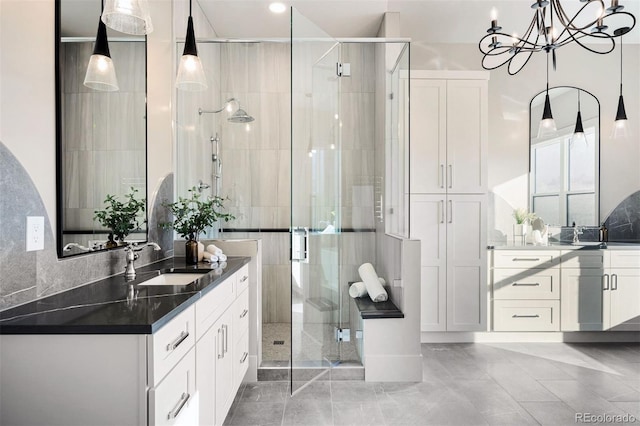 full bath with a sink, two vanities, an inviting chandelier, and a stall shower