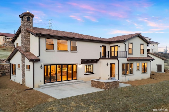 back of house featuring a tile roof, stucco siding, a chimney, a balcony, and a patio area