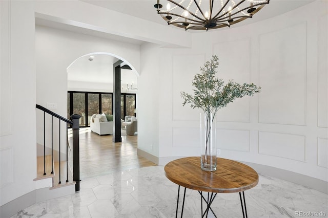 corridor featuring an inviting chandelier, a decorative wall, arched walkways, and marble finish floor