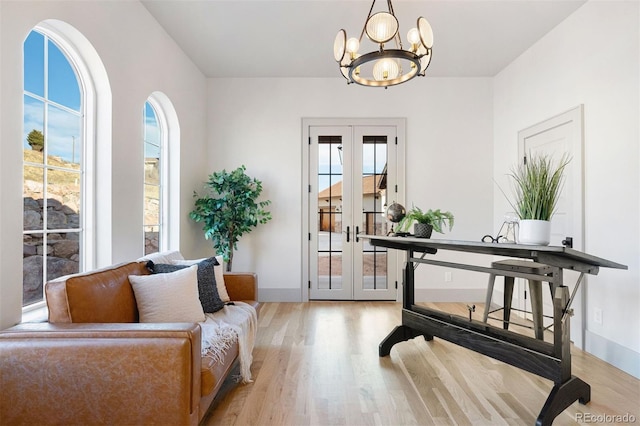 living area featuring a notable chandelier, french doors, light wood-style floors, and baseboards