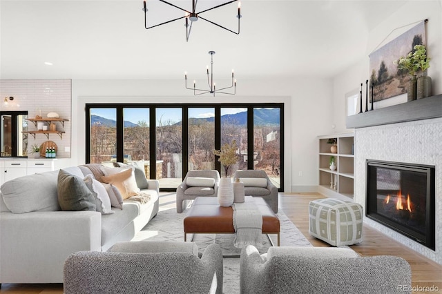 living room with a chandelier, a glass covered fireplace, light wood-type flooring, and baseboards