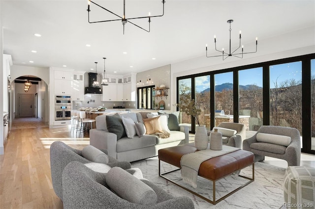 living area featuring arched walkways, light wood-style floors, and an inviting chandelier