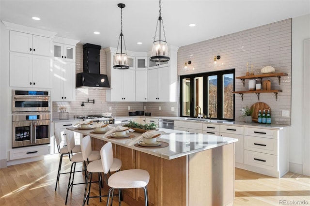 kitchen with tasteful backsplash, a kitchen island, stainless steel appliances, wall chimney exhaust hood, and light wood finished floors