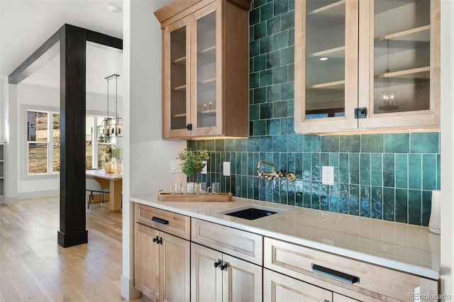 bar featuring light wood-type flooring, tasteful backsplash, and a sink