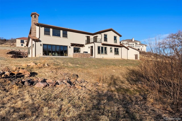 rear view of property with stucco siding, a chimney, a lawn, and a balcony