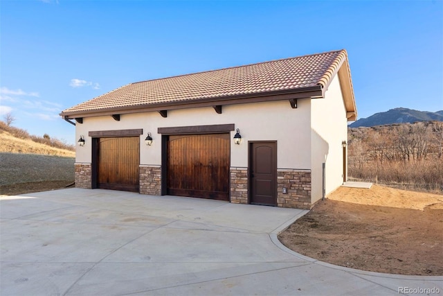 view of front facade featuring a tile roof, stucco siding, a garage, stone siding, and a mountain view