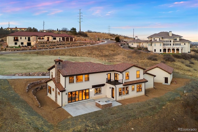 back of house with a balcony, a patio area, a chimney, and stucco siding