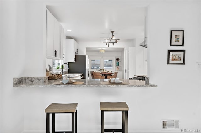 kitchen featuring kitchen peninsula, white cabinets, light stone counters, and stainless steel fridge