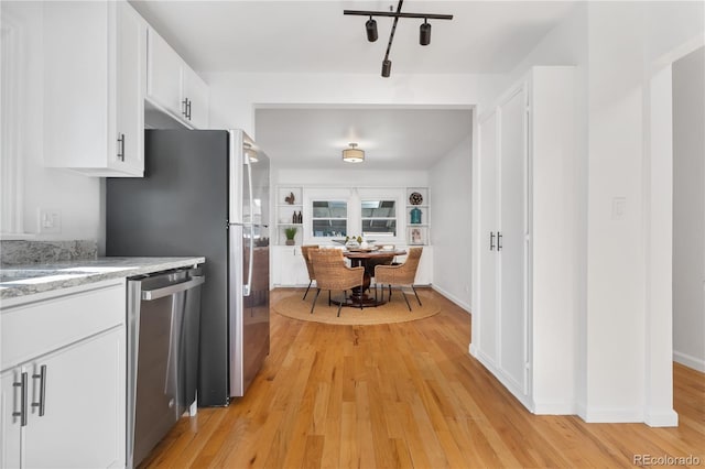 kitchen with stainless steel dishwasher, white cabinets, light wood-type flooring, and light stone counters