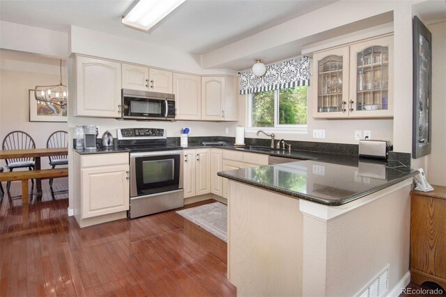 2935 Bow Line Pl, Longmont, CO 80503 - kitchen with appliances with stainless steel finishes, a chandelier, a peninsula, glass insert cabinets, and dark wood-type flooring