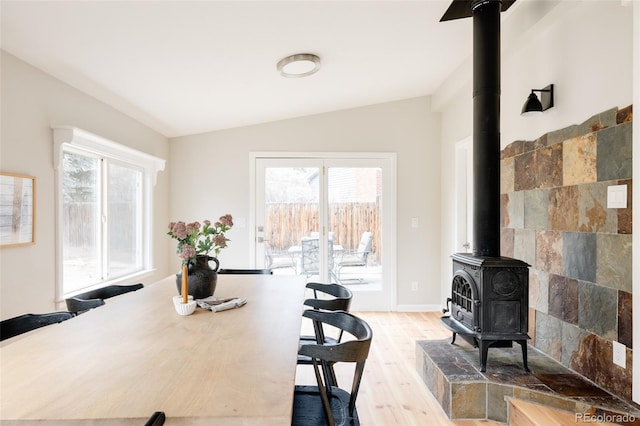 dining space featuring lofted ceiling, hardwood / wood-style floors, a healthy amount of sunlight, and a wood stove