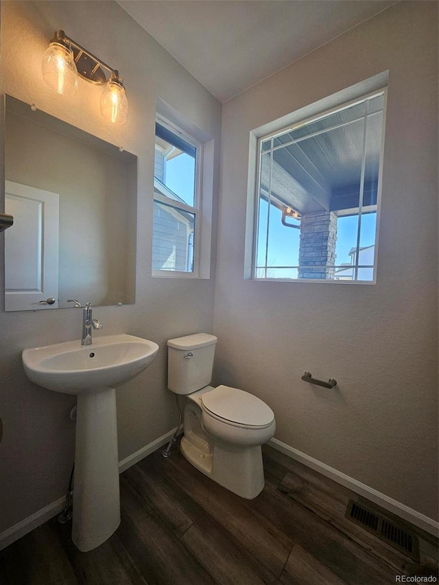 bathroom with baseboards, visible vents, toilet, and wood finished floors