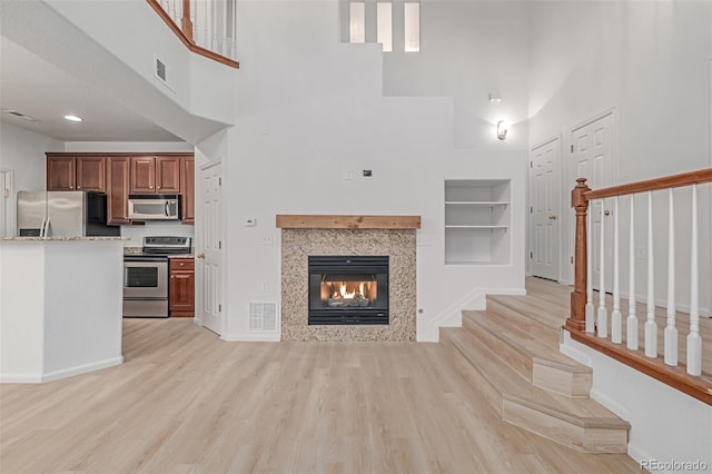 7777 E 23rd Ave Unit 1406, Denver, CO 80238 - unfurnished living room with a towering ceiling, stairway, a multi sided fireplace, built in features, and light wood-type flooring