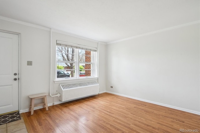 foyer with light wood-style floors, radiator, ornamental molding, and baseboards