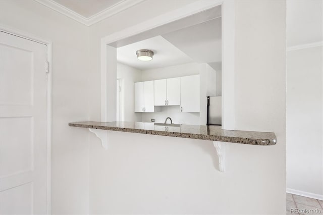 kitchen with freestanding refrigerator, white cabinetry, stone counters, and a kitchen bar