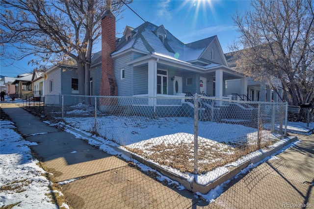 view of front of house featuring covered porch, a fenced front yard, and a chimney