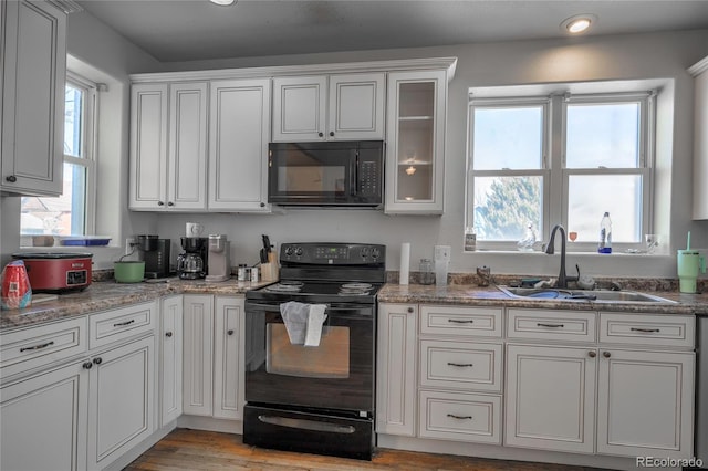 kitchen featuring sink, black appliances, light hardwood / wood-style flooring, light stone countertops, and white cabinets