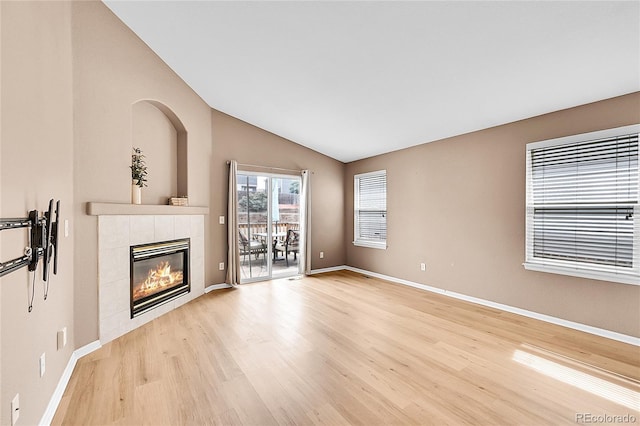 unfurnished living room with light wood finished floors, baseboards, vaulted ceiling, and a tiled fireplace