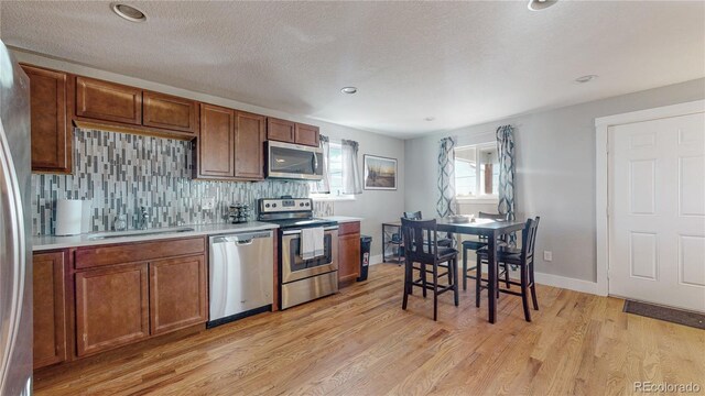 kitchen with sink, light hardwood / wood-style flooring, stainless steel appliances, a textured ceiling, and decorative backsplash