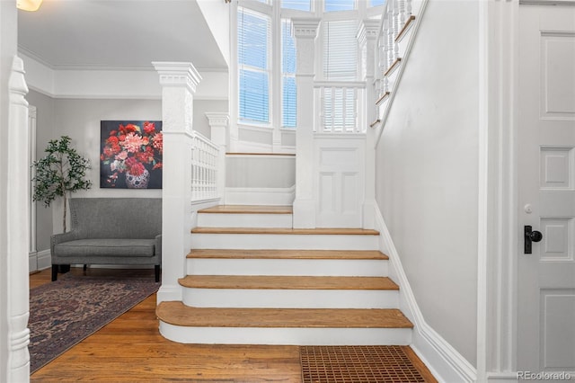 staircase featuring crown molding, wood-type flooring, and decorative columns