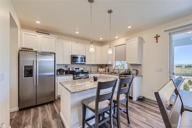 kitchen with dark wood finished floors, stainless steel appliances, white cabinetry, a sink, and a kitchen island