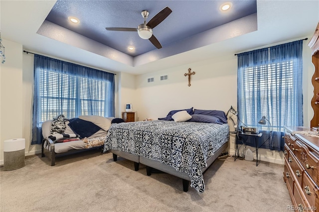 bedroom with light carpet, visible vents, and a tray ceiling