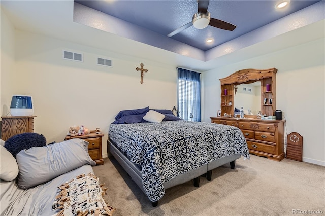 bedroom with a raised ceiling, visible vents, and light carpet