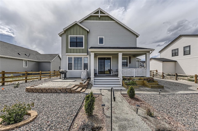 view of front of property featuring board and batten siding, covered porch, a patio, and fence