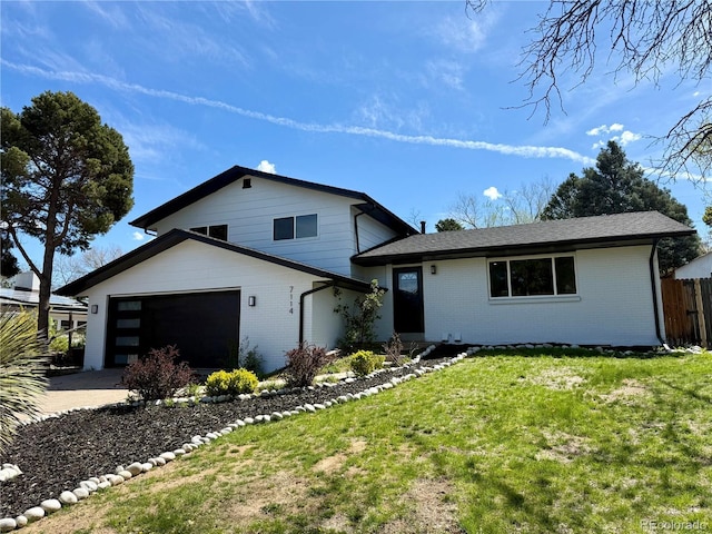 split level home featuring an attached garage, fence, a front yard, brick siding, and driveway