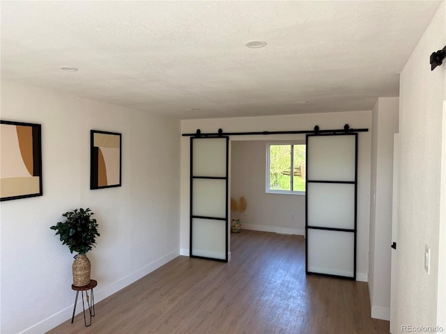 spare room featuring a barn door, baseboards, and wood finished floors