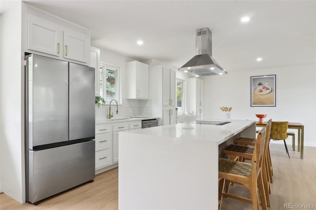 kitchen featuring a breakfast bar area, island exhaust hood, light wood-style flooring, white cabinets, and appliances with stainless steel finishes