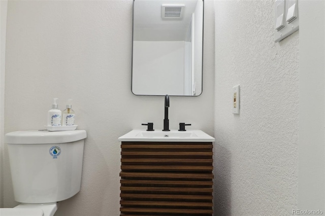 bathroom with toilet, vanity, visible vents, and a textured wall
