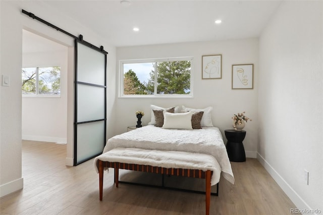bedroom with light wood-style floors, a barn door, and baseboards
