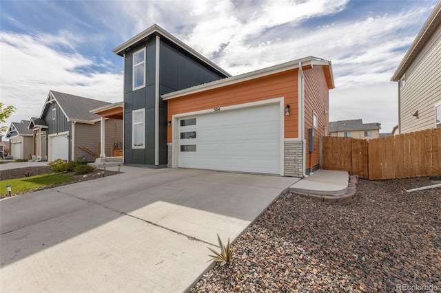 contemporary home with stone siding, an attached garage, driveway, and fence