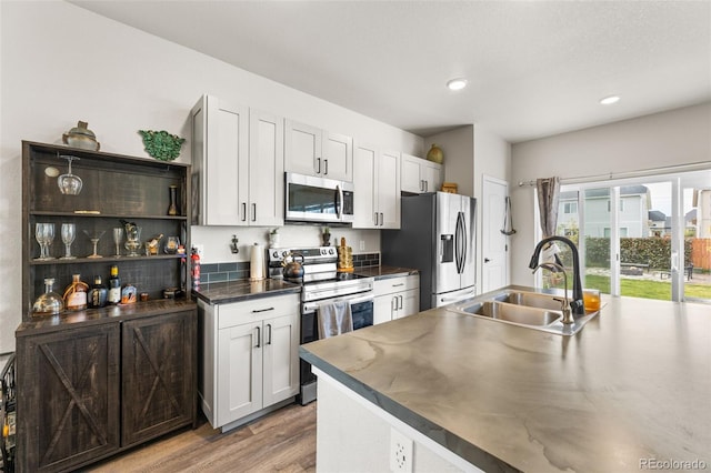 kitchen with dark countertops, light wood finished floors, recessed lighting, stainless steel appliances, and a sink