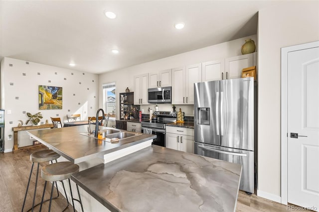 kitchen featuring a breakfast bar area, light wood-style flooring, an island with sink, a sink, and appliances with stainless steel finishes